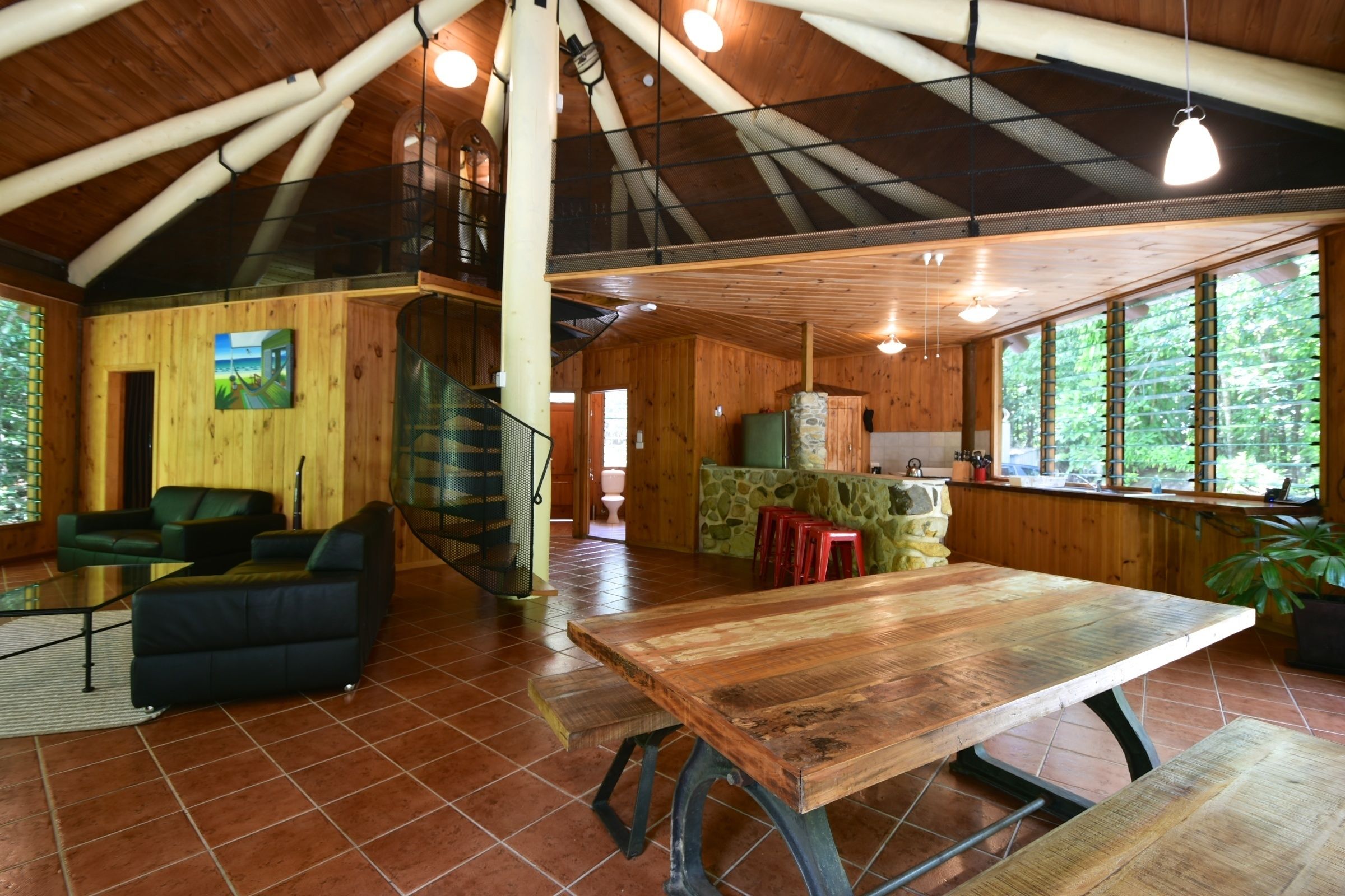 A spacious wooden interior with a large dining table, a sofa, and a staircase leading to an upper level.