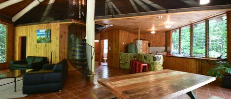 A spacious wooden interior with a large dining table, a sofa, and a staircase leading to an upper level.