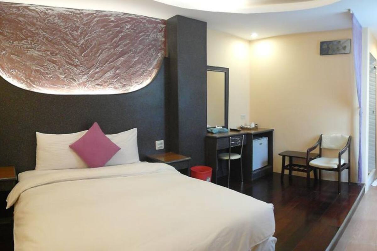 A hotel room with a bed, a desk, a chair, and a mirror.