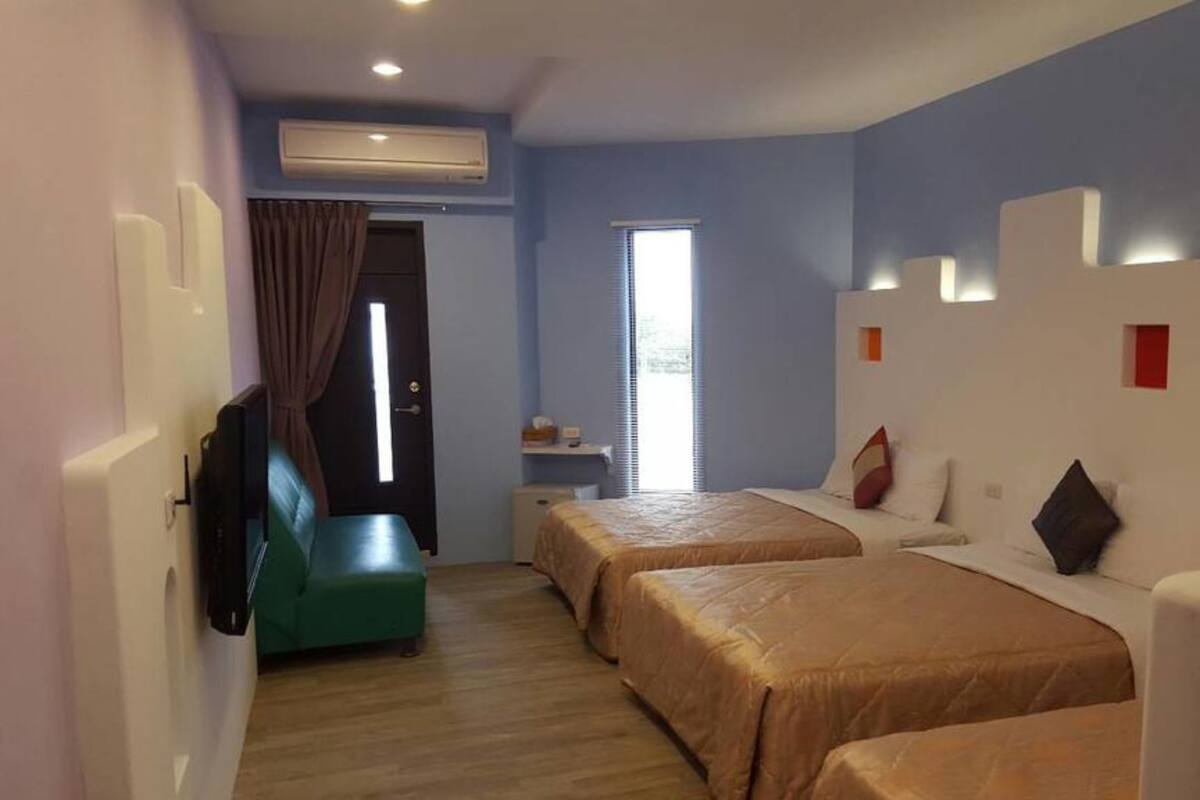 A hotel room with two beds, a small desk, a chair, and a window with blinds.
