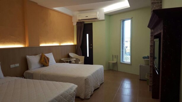 A hotel room with two beds, a small table, a chair, a window with blinds, and an air conditioning unit. - Kenting Sea Cloudless Day Home (Hengchun)
