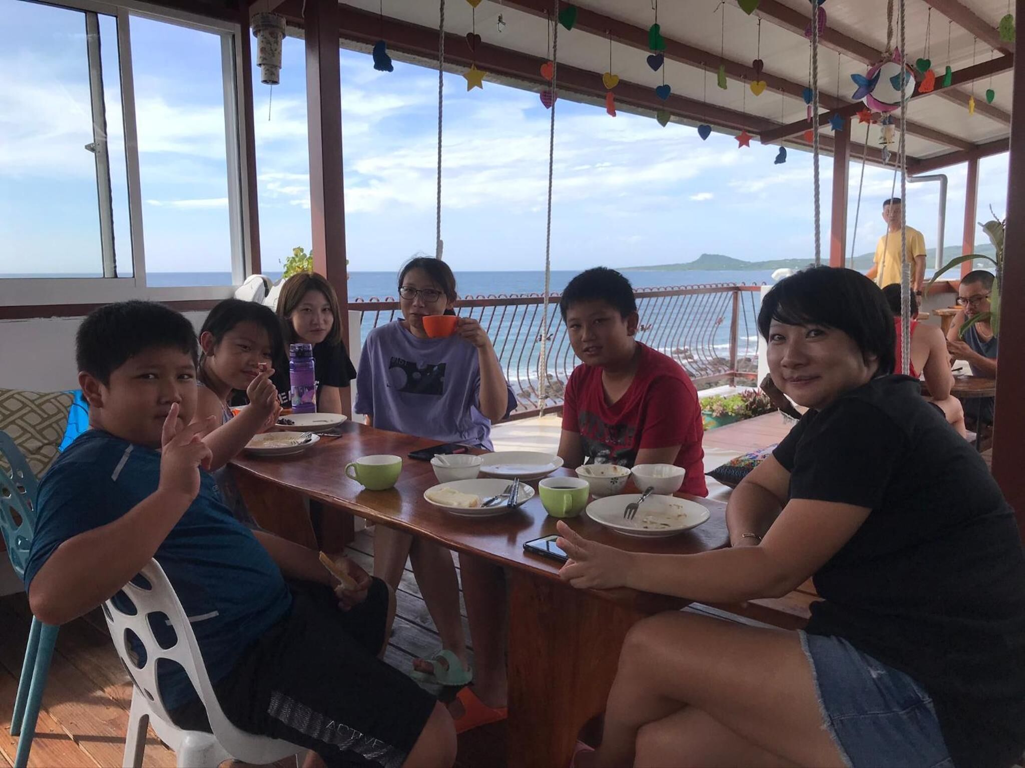 A group of people dining at a wooden table with a view of the sea.