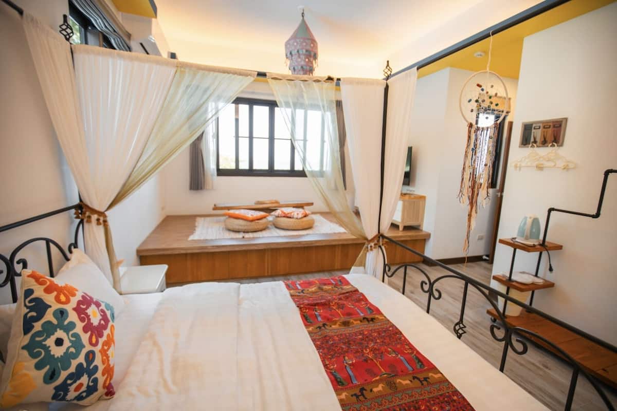 A bedroom with a bed, a canopy, a red rug, and a dreamcatcher.