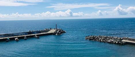 A pier extending into the sea with a lighthouse at the end, surrounded by calm waters and clear skies.