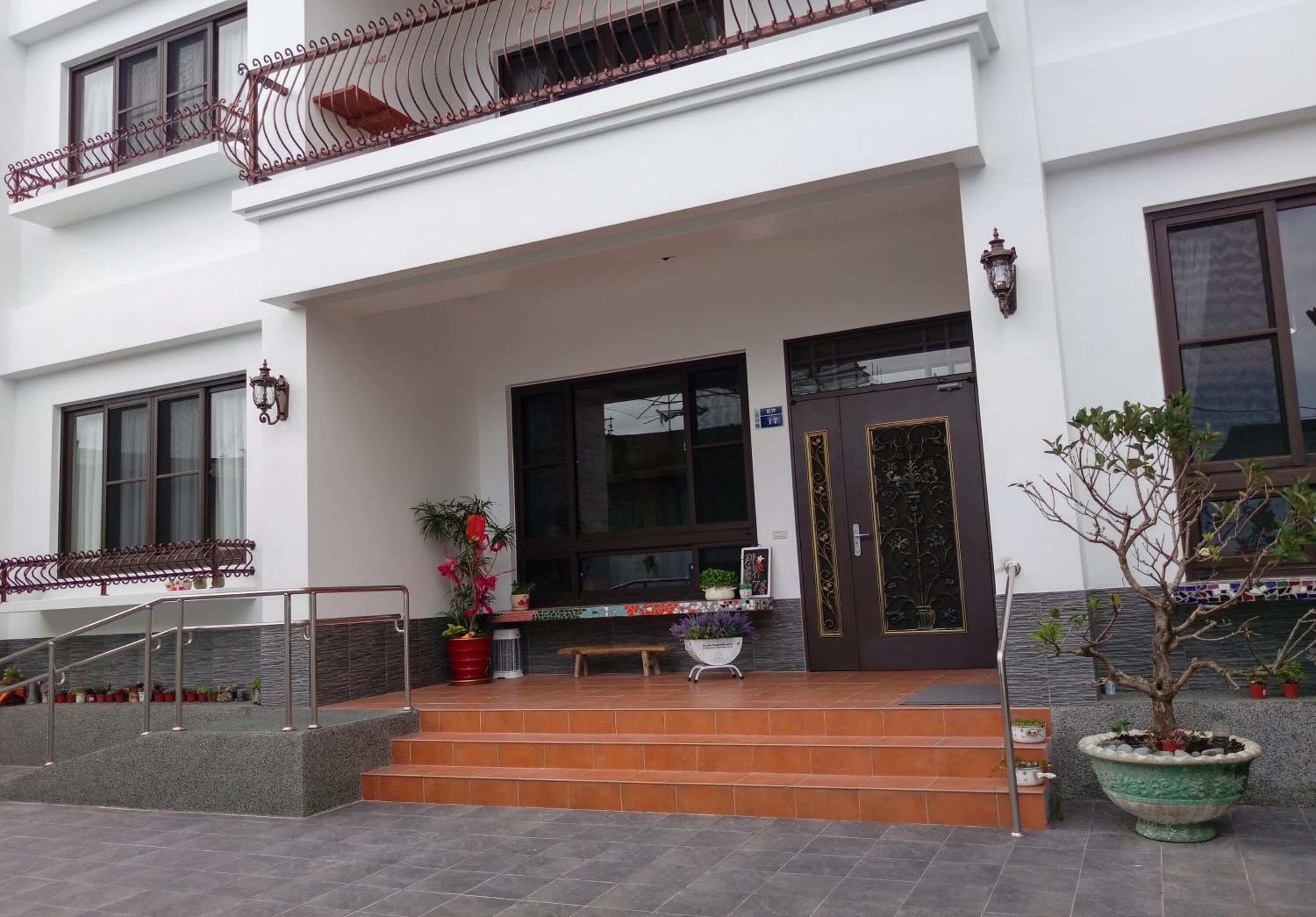 Ein Gebäude mit weißer Fassade, einem Balkon mit schmiedeeisernem Geländer, einer Haustür mit dekorativem Glasfeld und Stufen, die zum Eingang führen.