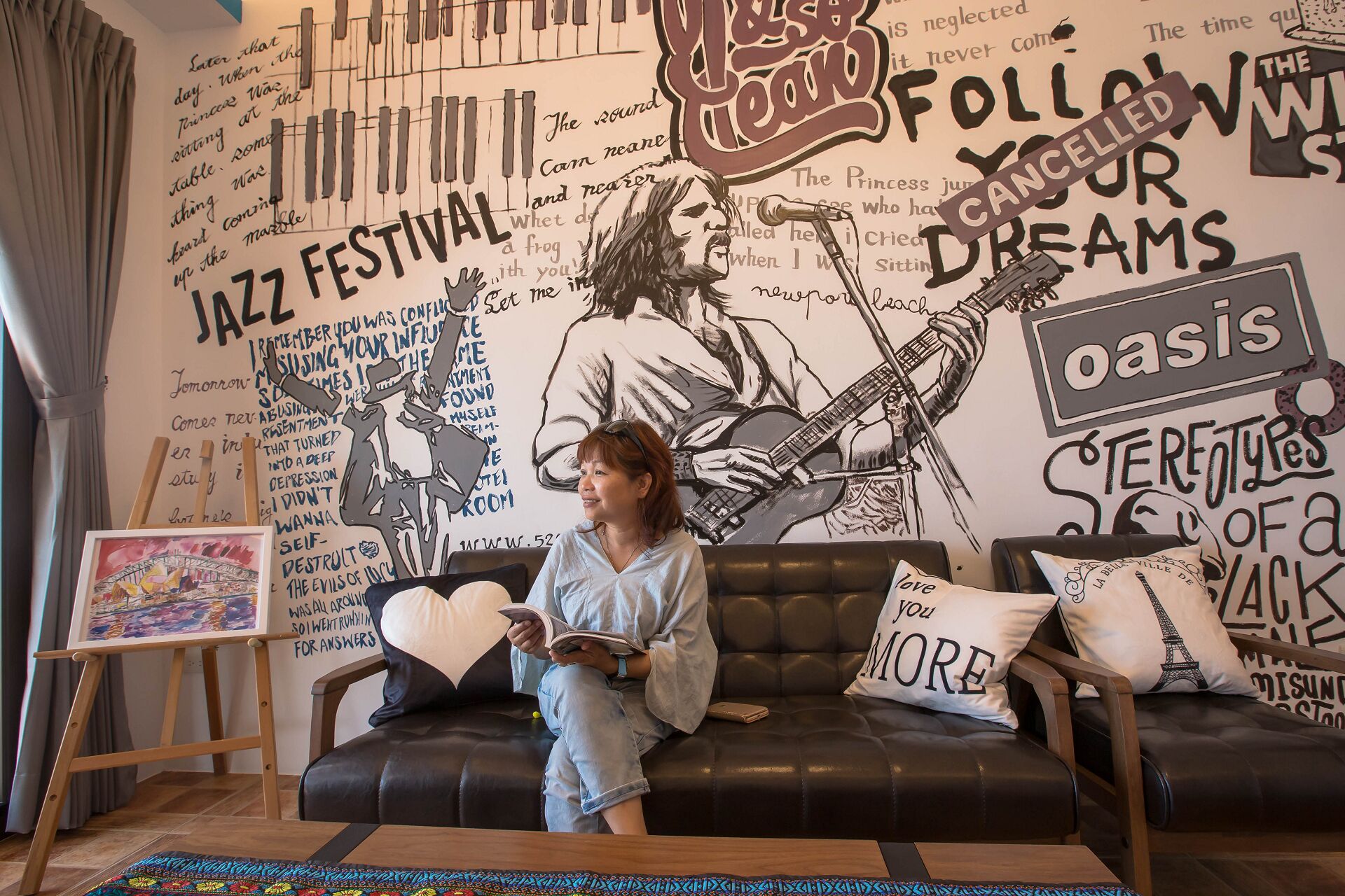 A person sitting on a couch in a room with a wall mural featuring musical instruments and text.