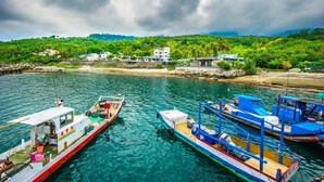 A marina with several boats docked, a rocky shoreline, and buildings in the background. - Najie (Donghe)