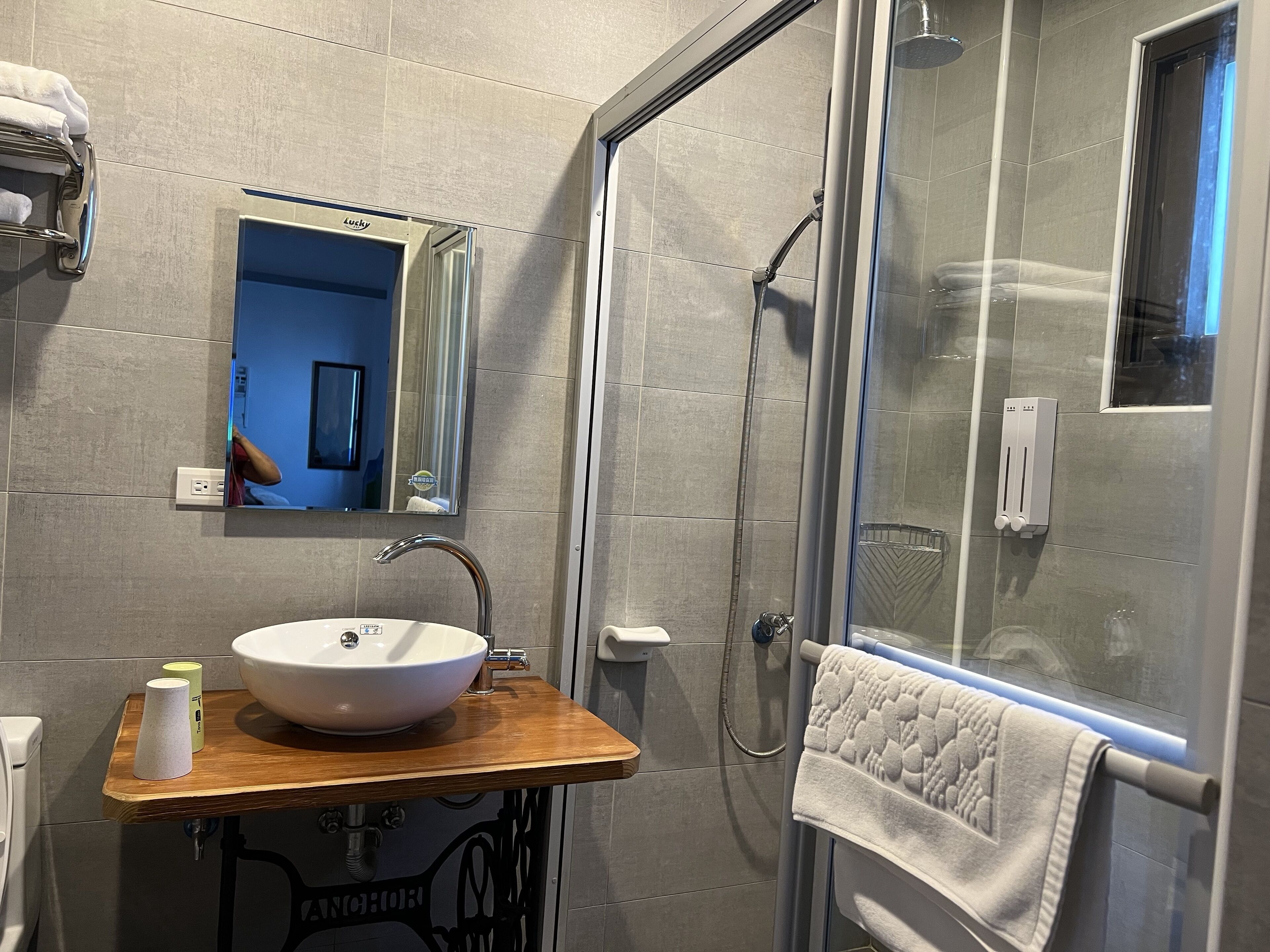 A bathroom with a wooden vanity, a white sink, a mirror, and a glass-enclosed shower.
