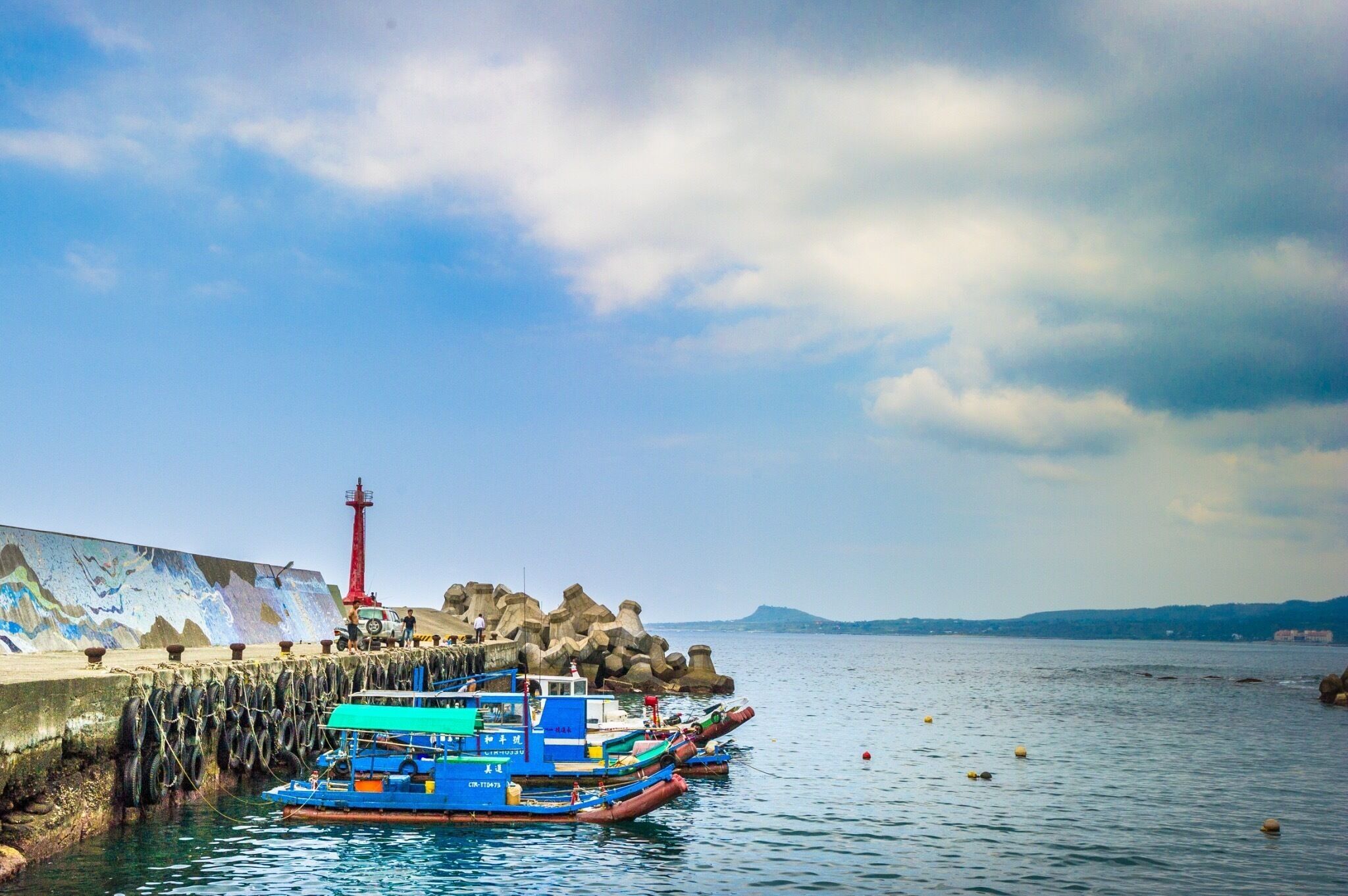 A pier with boats docked, a lighthouse, and a rocky shoreline.