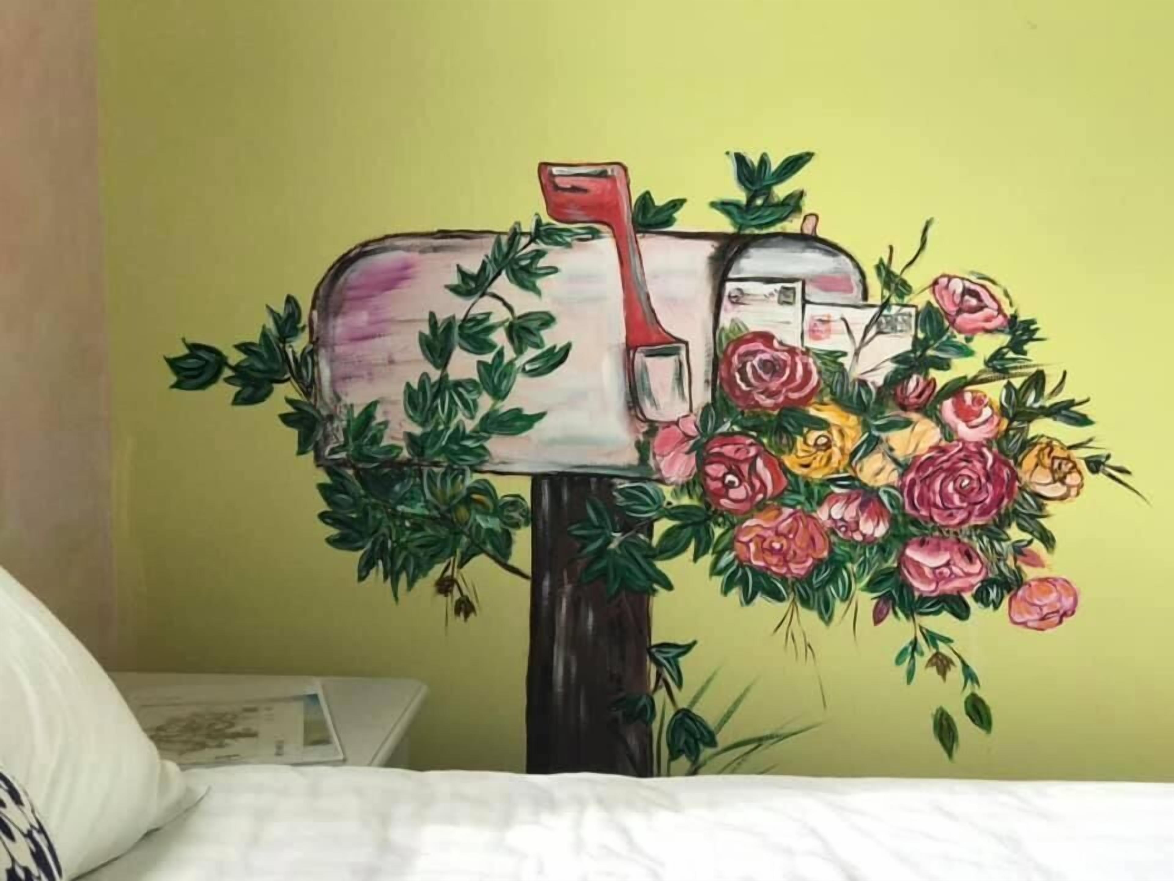 Una cassetta delle lettere con maniglia rossa e corpo bianco, decorata da verdeggiante vegetazione e fiori rosa e gialli.