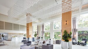 Een ruime lobby met een hoge plafond, grote ramen en modern meubilair.