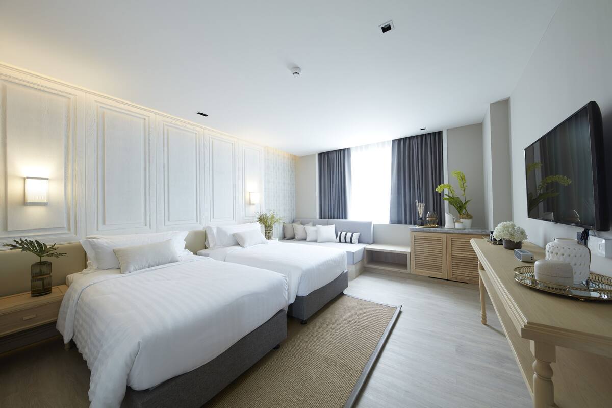 A modern hotel room with two beds, a seating area, a desk, and a large TV.
