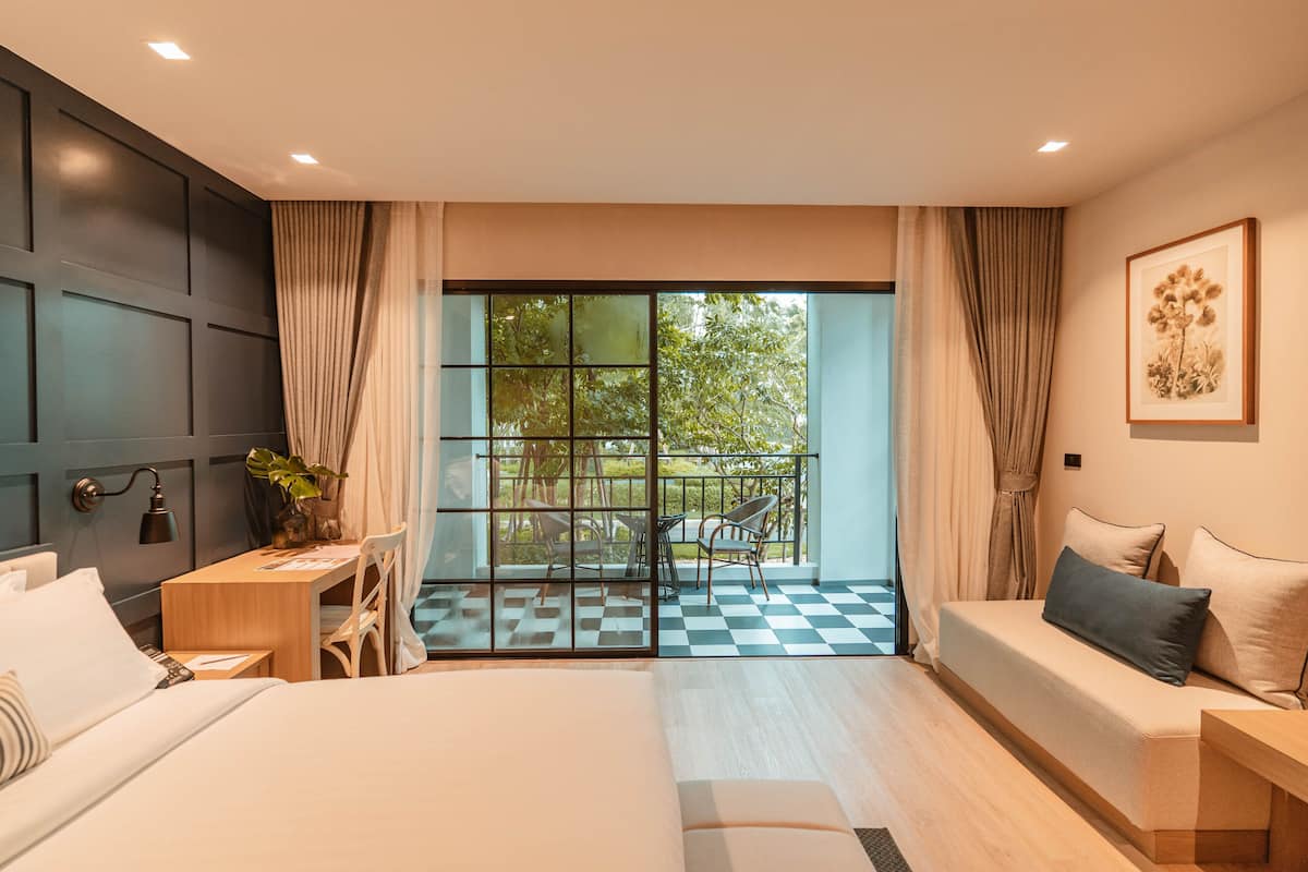 A modern hotel room with a large bed, a desk, and a balcony with a checkered floor.