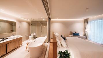 A modern hotel room with a large bed, a separate bathroom with a bathtub, a wooden vanity, and a large mirror.