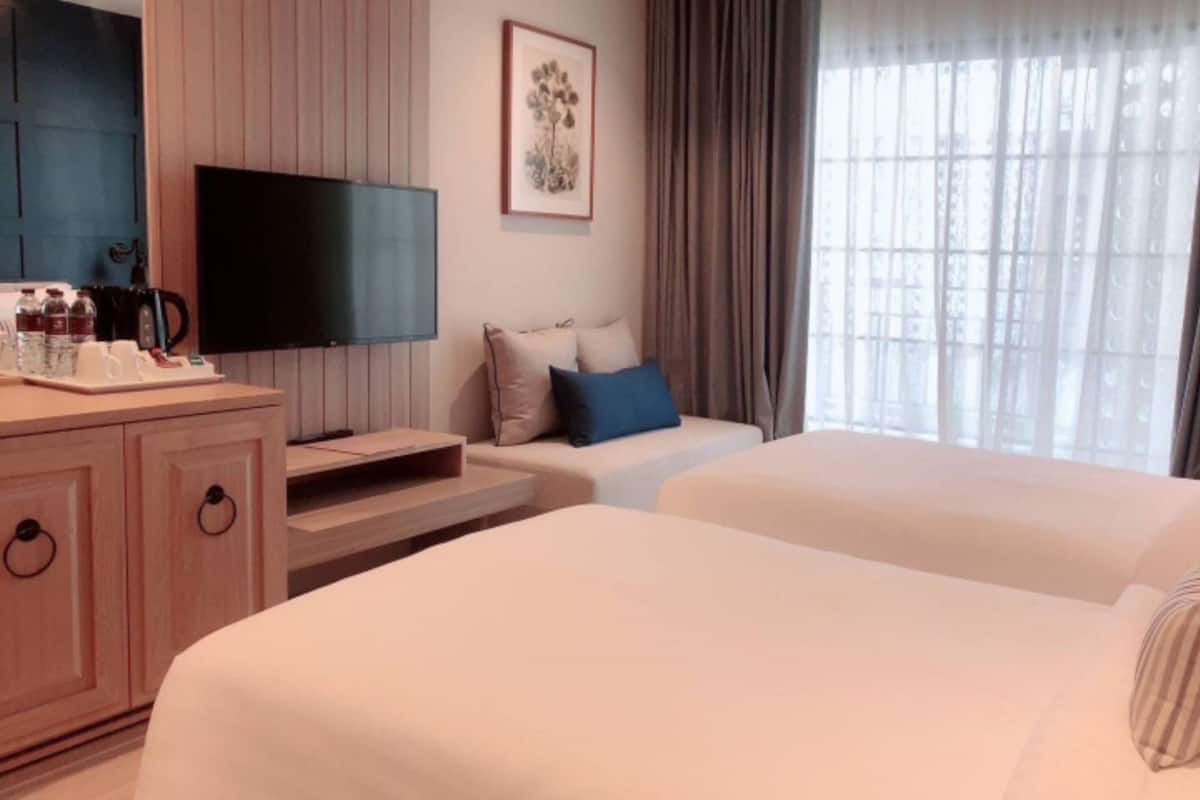 A hotel room with two beds, a TV, a desk with a coffee maker, and a window with curtains.