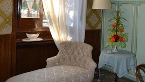 Una habitación con un sofá antiguo, una mesita con una lámpara y una ventana con cortinas.