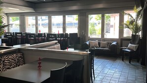 A spacious restaurant with high ceilings, large windows, and a mix of seating including tables and a sofa. - an Hotel (Selm)