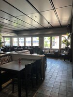 A spacious restaurant with high ceilings, large windows, and a mix of seating including tables and a sofa.