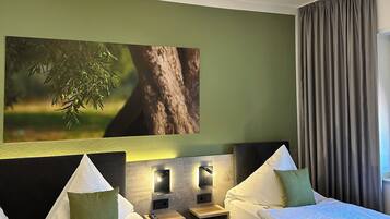 A hotel room with two beds, a green wall, a painting of a tree, and a window with curtains.