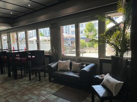 Un rincón acogedor con un sofá y sillones de cuero, ventanas amplias con vistas a la calle y una planta en maceta.