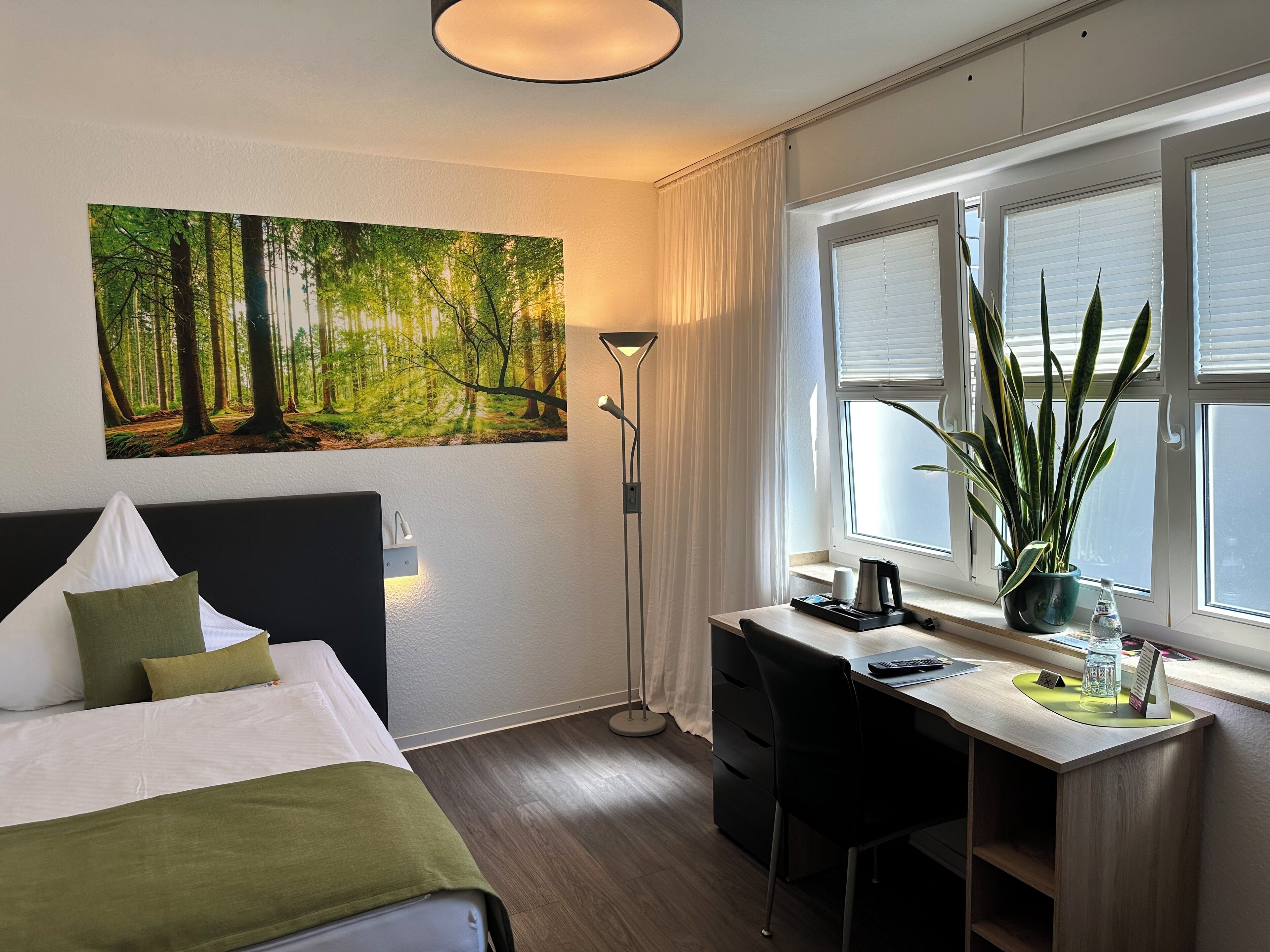 Habitación de hotel con cama, escritorio y un cuadro grande con tema de bosque en la pared.