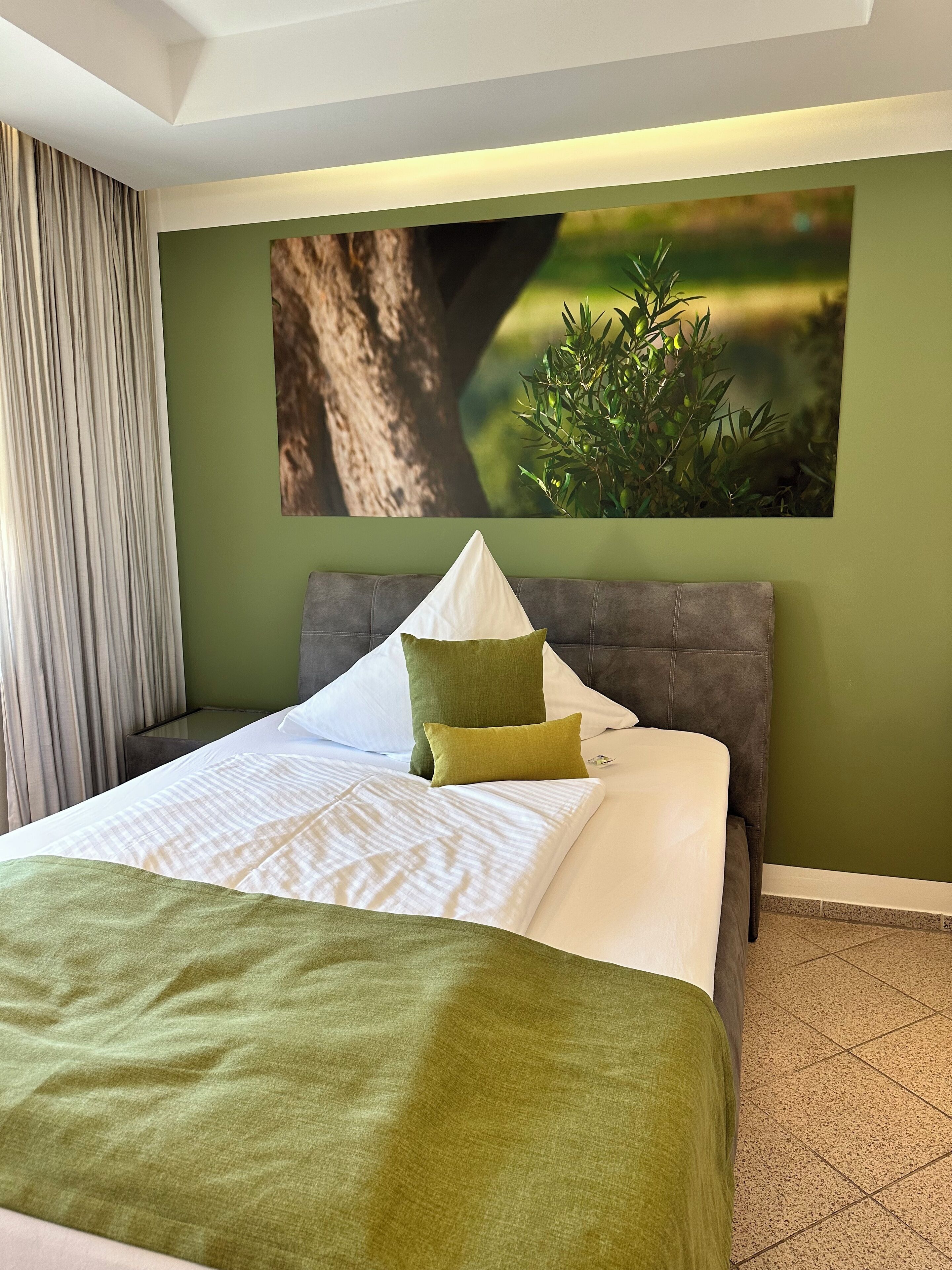 Un lit bien fait, avec une couvre-lit verte et blanche, une tête de lit rembourrée grise et un oreiller vert.