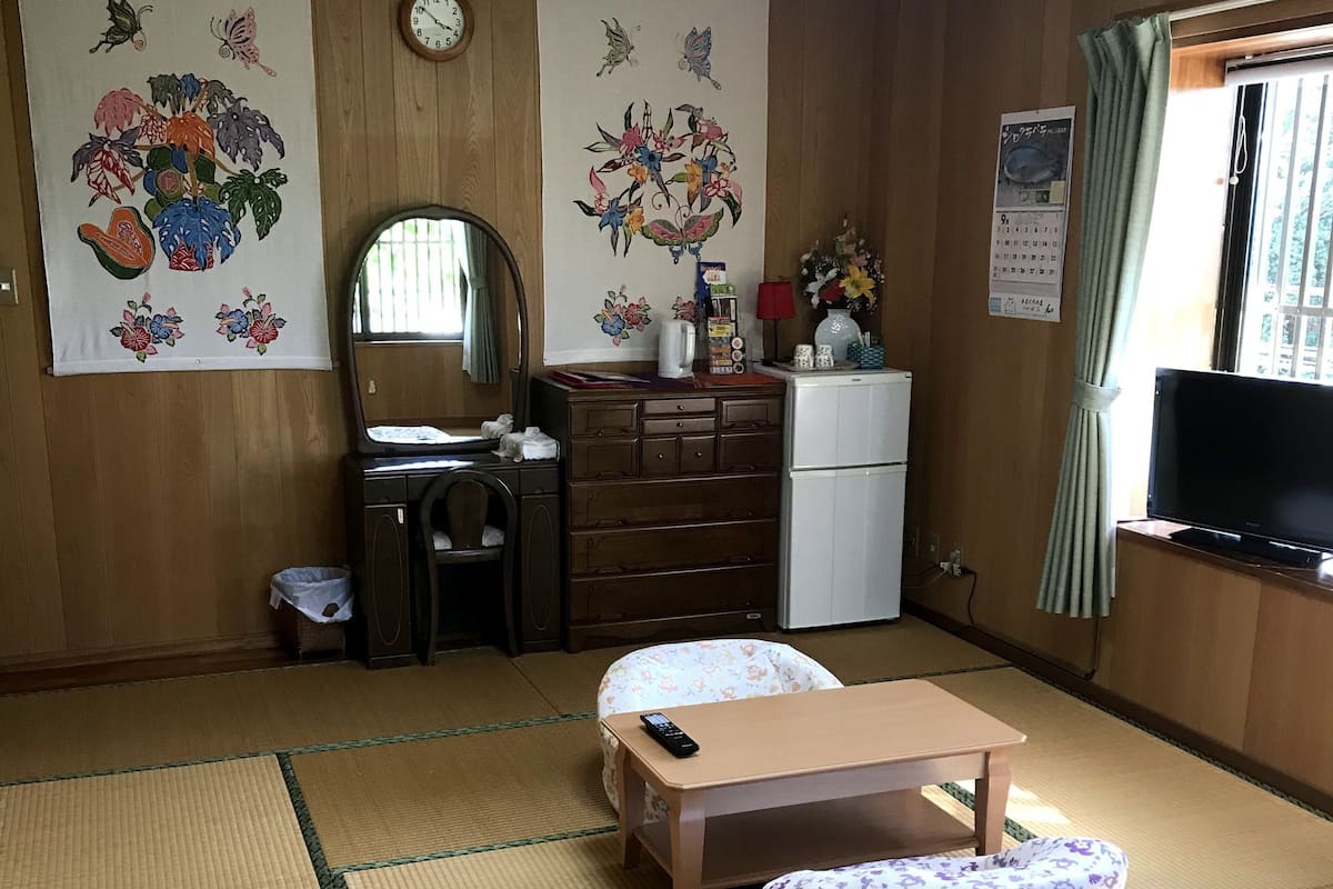 Ein traditioneller japanischer Raum mit Tatami-Böden, einem niedrigen Holztisch, einem Fernseher und dekorativer Wandkunst.