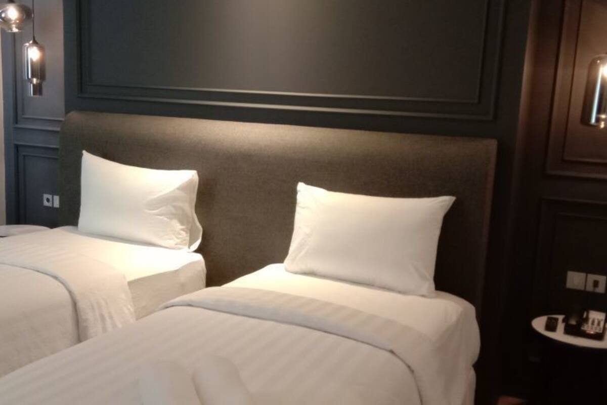 A hotel room with two beds, each with white linens and pillows, a dark headboard, and wall-mounted light fixtures.