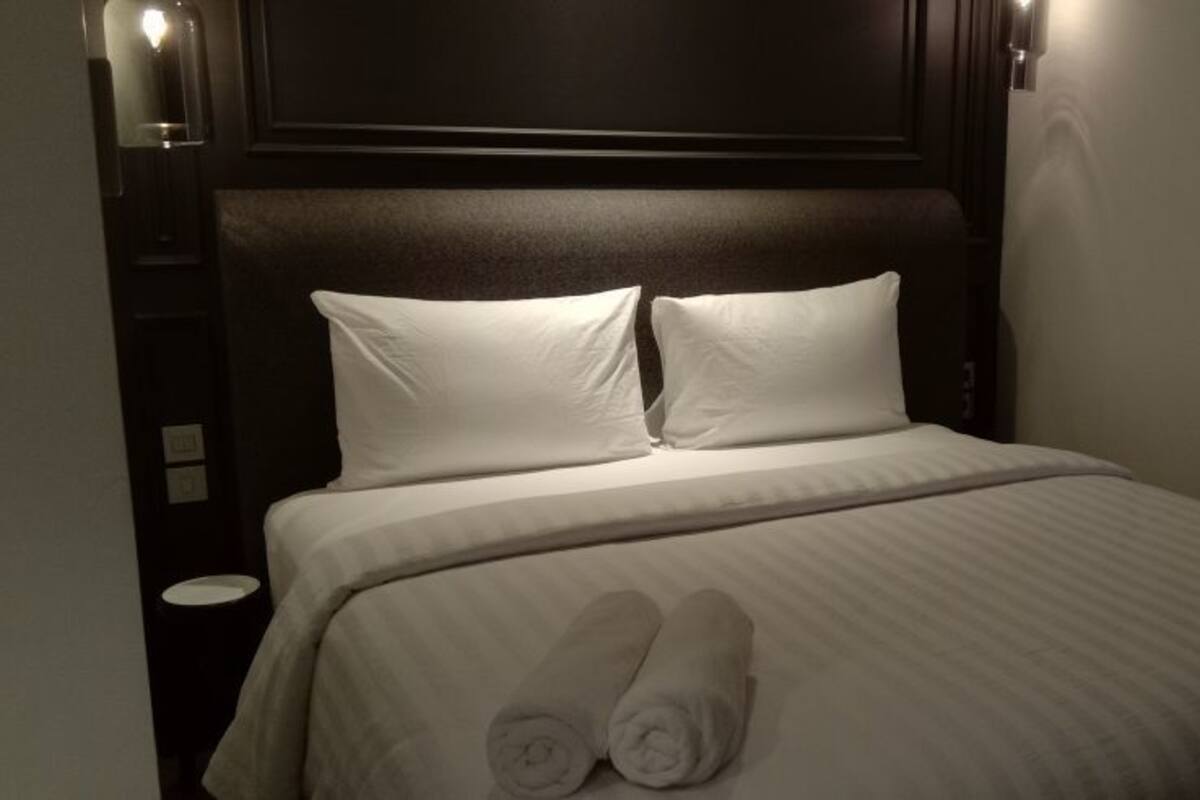 A neatly made bed with white linens and two rolled towels placed at the foot of the bed.