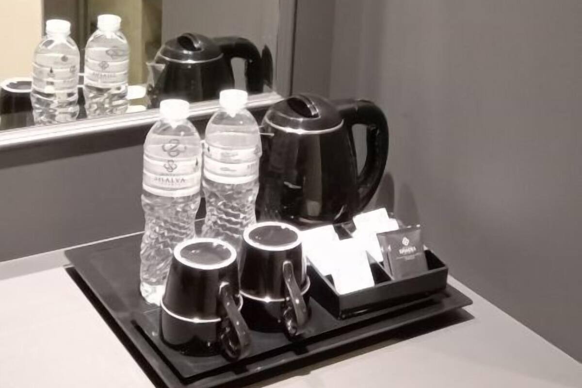 A hotel room with a minibar containing water bottles, a coffee maker, and cups.