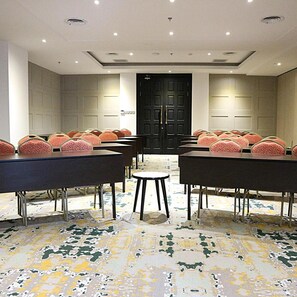 A conference room with tables and chairs, a patterned carpet, and a black door.