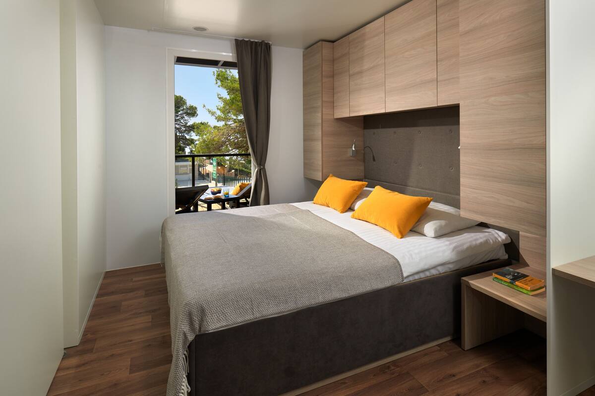 Une chambre à coucher moderne avec un grand lit, une tête de lit en bois et une petite table de chevet avec des livres.
