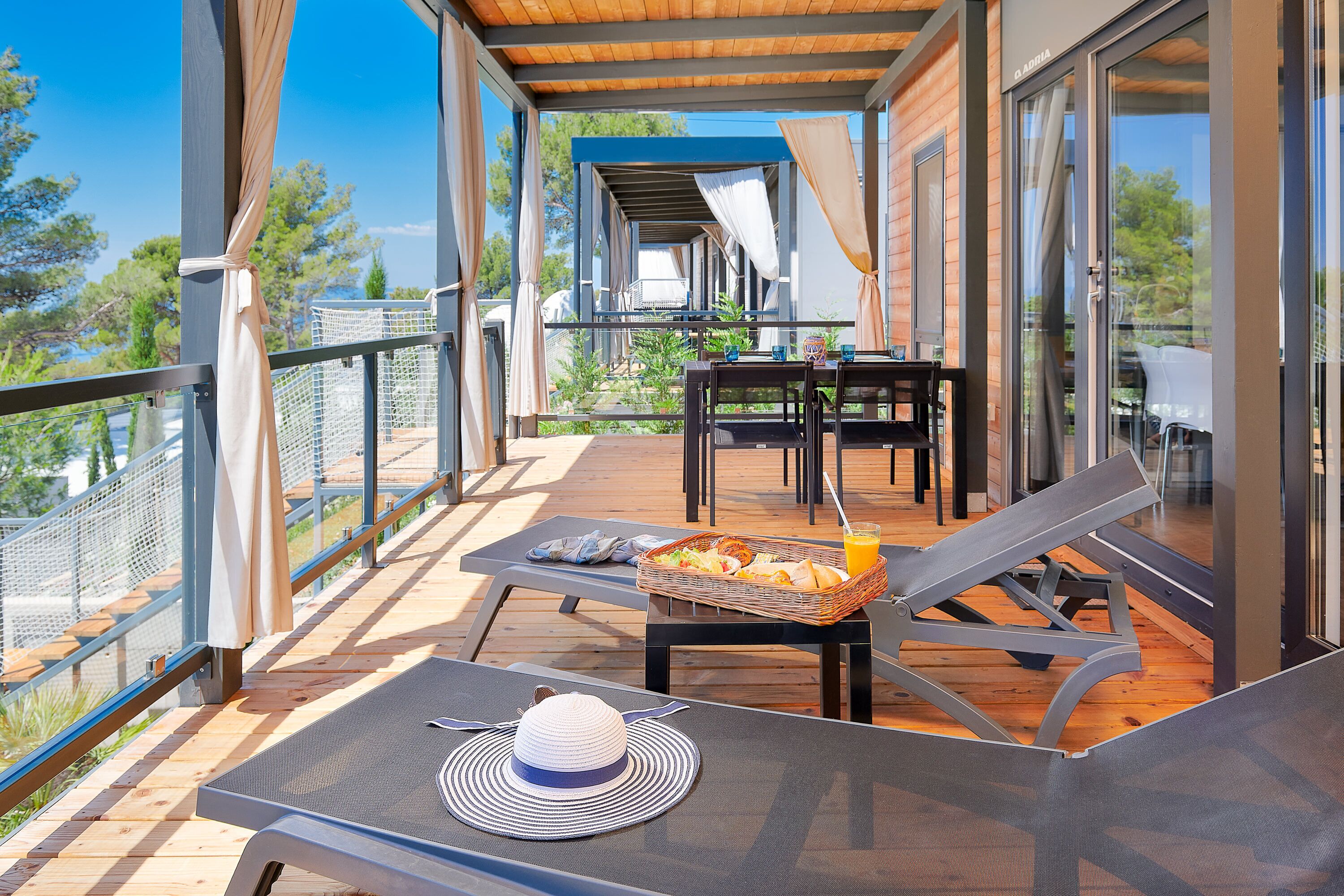 A balcony with a table set for breakfast, including a basket of food and a drink.