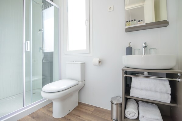 Un baño moderno con cabina de ducha de vidrio, inodoro blanco, lavamanos con espejo y repisa con toallas.