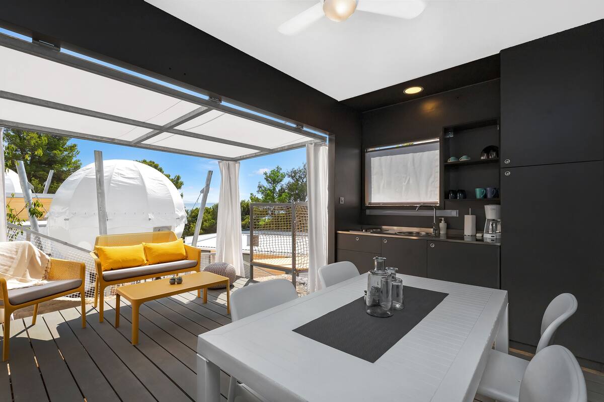 Une cuisine extérieure moderne dotée d’un espace repas, comprenant une table et des chaises, ainsi qu’un canapé avec des coussins.