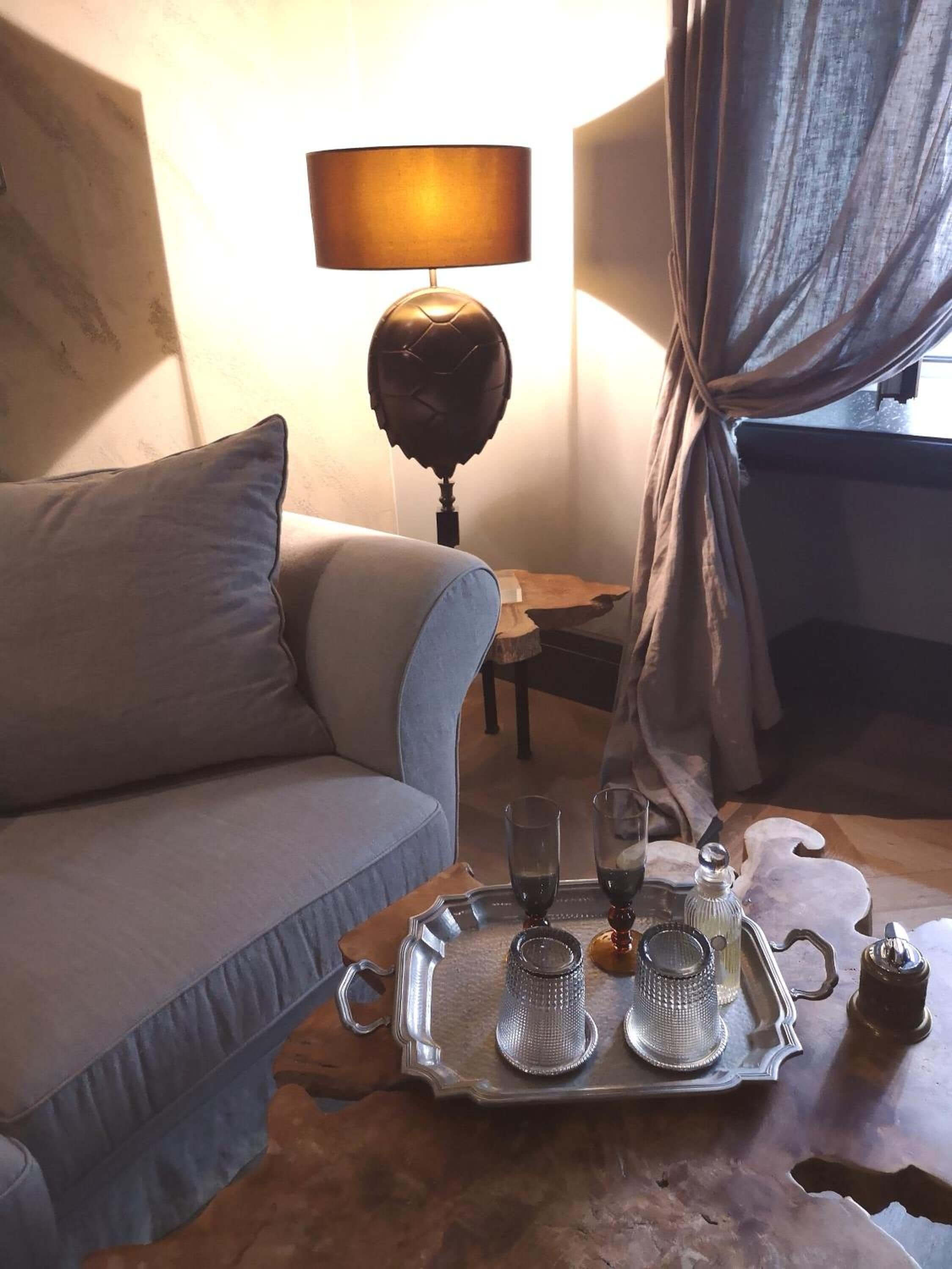 Une pièce confortable avec un canapé, une lampe et un plateau sur lequel se trouvent des verres et une bouteille.