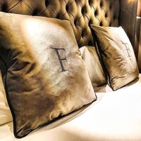 Cabecera tapizada con almohadones que presentan letras en relieve.