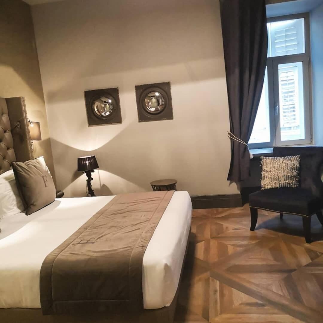 Habitación de hotel con una cama grande, una silla, una mesita pequeña y dos cuadros colgados en la pared.