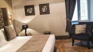 Habitación de hotel con una cama grande, una silla, una mesita pequeña y dos cuadros colgados en la pared.