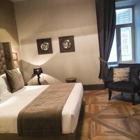 Habitación de hotel con una cama grande, una silla, una mesita pequeña y dos cuadros colgados en la pared.