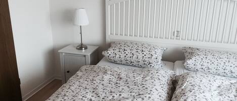 A bedroom with a white bed, a nightstand with a lamp, and a white headboard.
