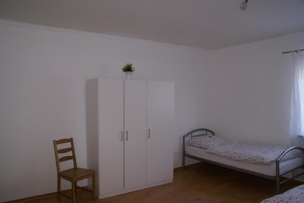Una habitación pequeña y poco amoblada, con una cama individual, una silla de madera y un armario blanco.