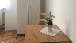 A room with a wooden table, a white wardrobe, a potted plant on the table, and a TV mounted on the wall. - Pension Lindenhof (Limburg an der Lahn)