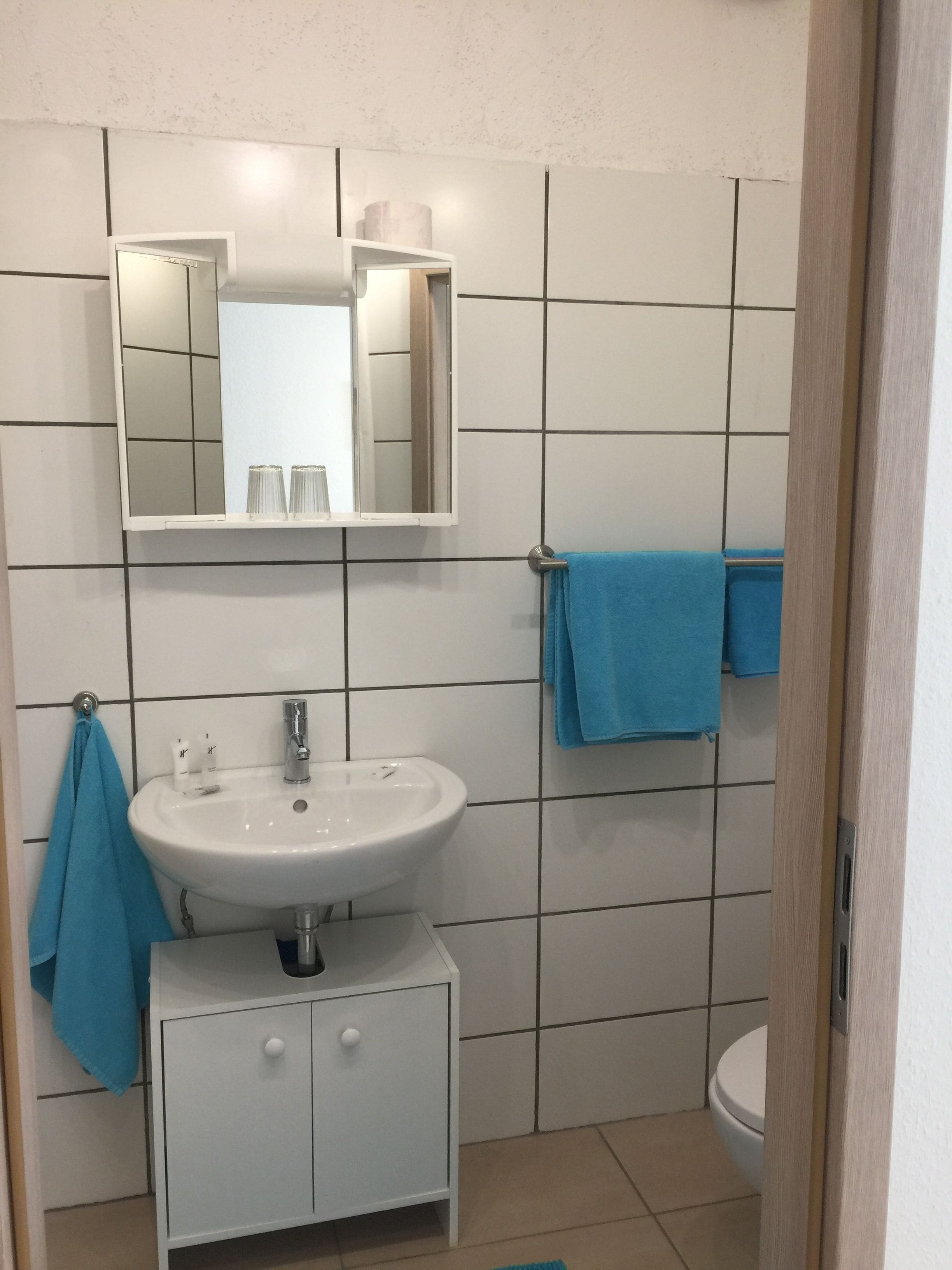 A bathroom with a white sink, mirror, and a toilet. There are two blue towels hanging on the wall.