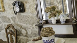 A stone wall with a vintage telephone, a wooden chair, and a table with a floral-patterned cup and saucer.
