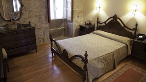 A bedroom with a wooden bed, a dresser, a mirror, and two wall sconces.