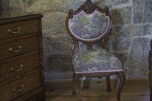 A wooden dresser with ornate handles and a chair with a floral upholstery against a stone wall. - Casa de Turismo Rural Os Petroglifos (Boiro)