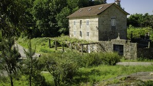 A stone building with a tiled roof, surrounded by lush greenery and trees.