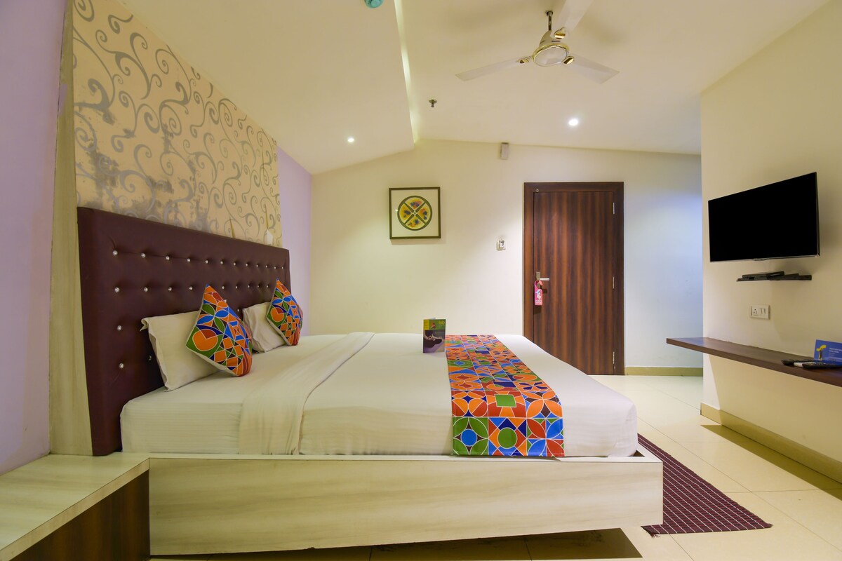 A hotel room with a large bed, a ceiling fan, a television, and a wooden door.