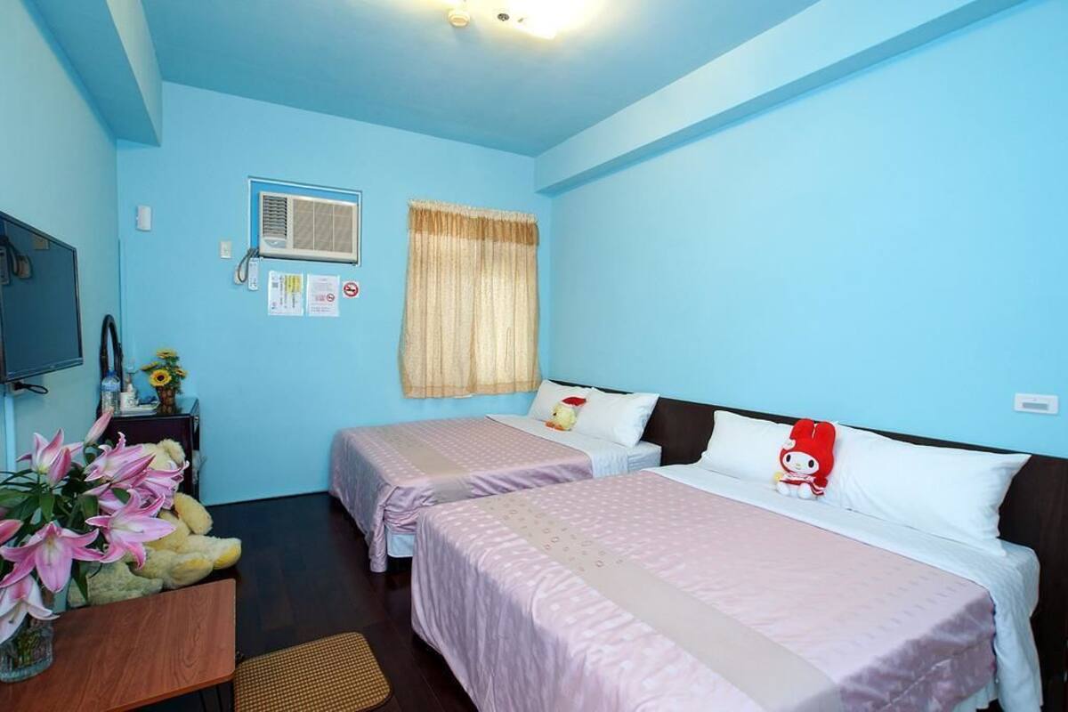 Habitación con dos camas, un televisor, una ventana con cortinas y una mesita con un jarrón de flores.